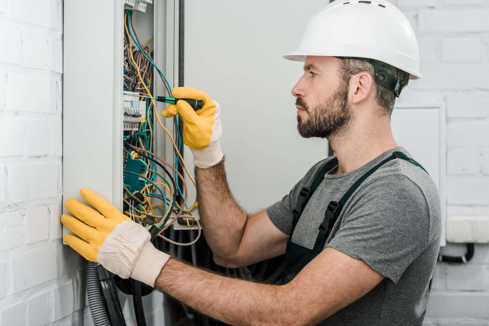 side view of handsome bearded electrician repairing electrical box and using screwdriver in corridor